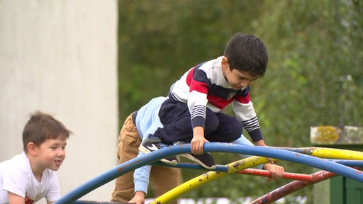 Mehrere Kinder klettern über ein Klettergrüst auf einem Spielplatz.