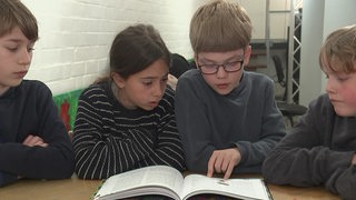 Vier Kinder lesen in einem Buch.
