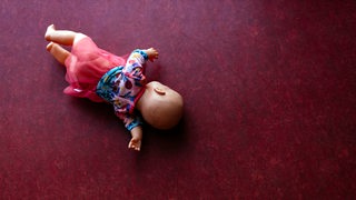 Eine Puppe liegt auf einem roten Teppich.