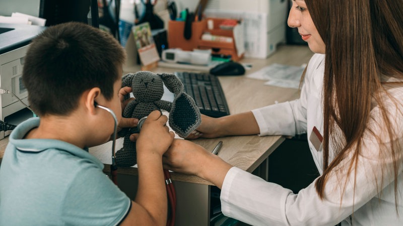 Eine Kinderärztin untersucht mit einem Kind ein Kuscheltier.