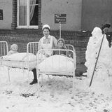 Kranke Kinder liegen auf ihren Betten vor dem Krankenhaus. Es hat geschneit.