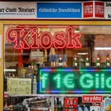 Das Schaufenster eines Kiosk auf den Kölner Ringen. Dort stehen Sektflaschen, Puppen und Werbung für "Coffee to go".