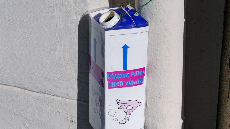 Ein Tetrapack hängt an einer Laterne, darauf steht: "Kippen bitter hier rein!" 