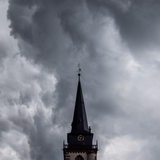 Dunkle Wolken eines Schauers sind am Abend am Himmel über einem Kirchturm zu sehen.