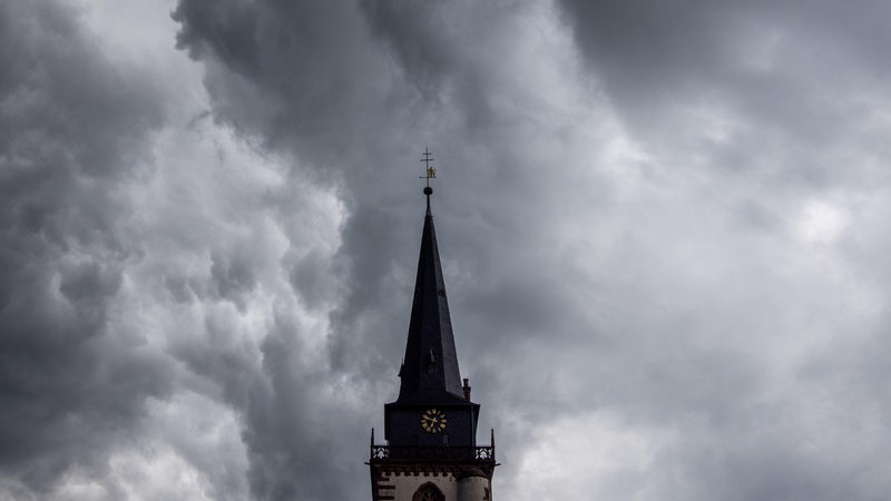 Dunkle Wolken eines Schauers sind am Abend am Himmel über einem Kirchturm zu sehen.