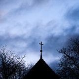 Dunkle Wolken ziehen über das Kreuz auf einer evangelischen Kirche in der Region Hannover hinweg. 