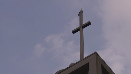 Die Spitze eines Kirchenturms mit Kreuz, auf dem ein Vogel sitzt