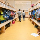 Zwei Jungen laufen aus einer Umkleide einer Kita. An den Garderoben hängen Jacken und Rucksäcke.