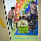 Erzieherinnen mit Kindern in einer Kinderkrippe, vorne an der Tür ein Hinweis an der Tür an die Eltern, draußen zu bleiben (Symbolbild)