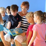 Eine Erzieherin liest den Kindergartenkindern aus einem Buch vor