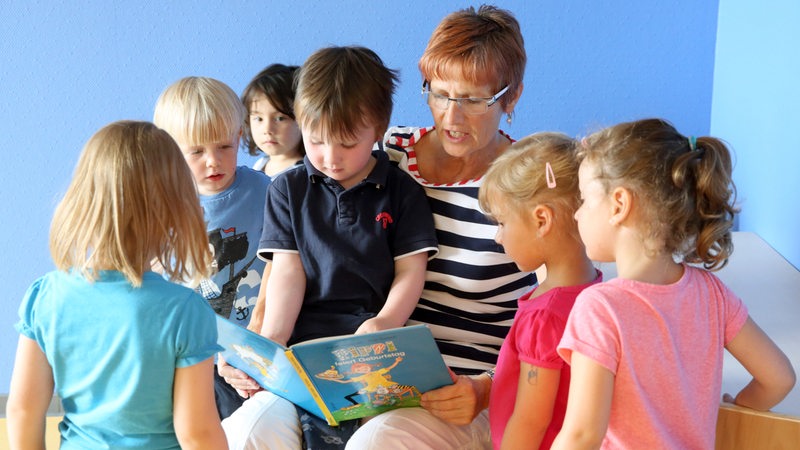 Eine Erzieherin liest den Kindergartenkindern aus einem Buch vor