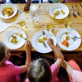 Kinder sitzen an einem Tich und vor ihnen stehen Teller mit Essen.