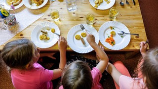 Kinder sitzen an einem Tich und vor ihnen stehen Teller mit Essen.