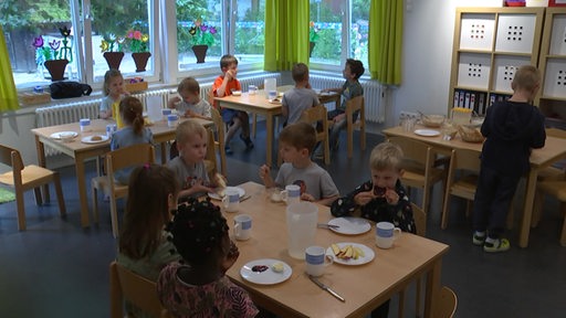 In einer Kindertagesstätte sitzen einige Kinder an Tischen während des Frühstücks. 