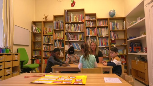 Kinder sitzen in einer Kita an einem Tisch vor Bücherregalen