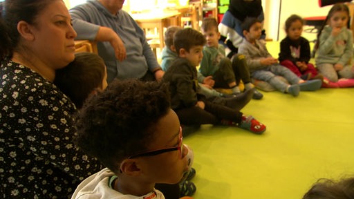 Mehrere Kinder sitzen auf dem Boden in einer Kita