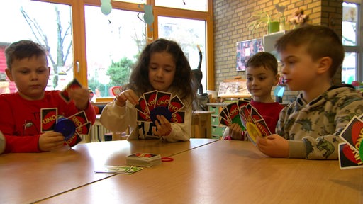 Vier Kinder sitzen gemeinsam an einem Tisch und spielen ein Kartenspiel.