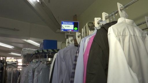 Viele Kleidungsstücke hängen auf Kleiderstangen in einer Wäscherei.
