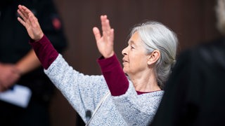 Daniela Klette hebt die Hände im Gerichtssaal.