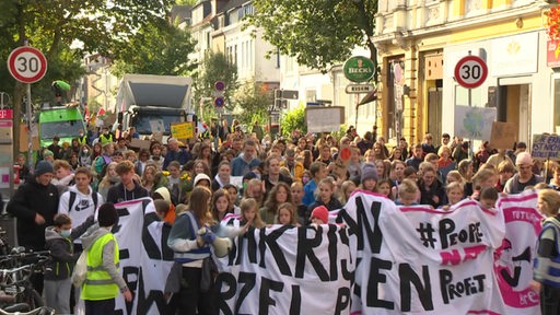 Mehrere Menschen laufen, mit Plakaten und Banner, auf der Klimademo durch das Bremer Viertel.