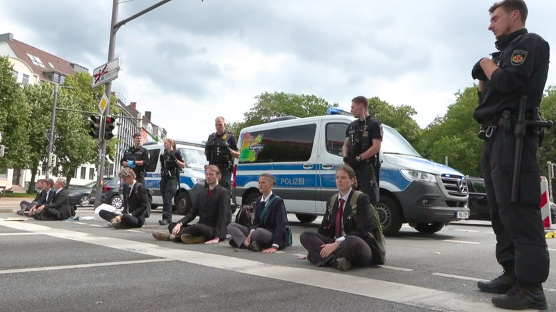 Zu sehen sind Mitglieder der letzten Generatiojn, welche sich an die Straße geklebt haben und von Polizisten umgeben sind.