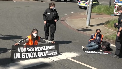 Klimaaktivistinnen mit einer Sitzblockade und Bannern auf der Straße. Die Polizei ist vor Ort.