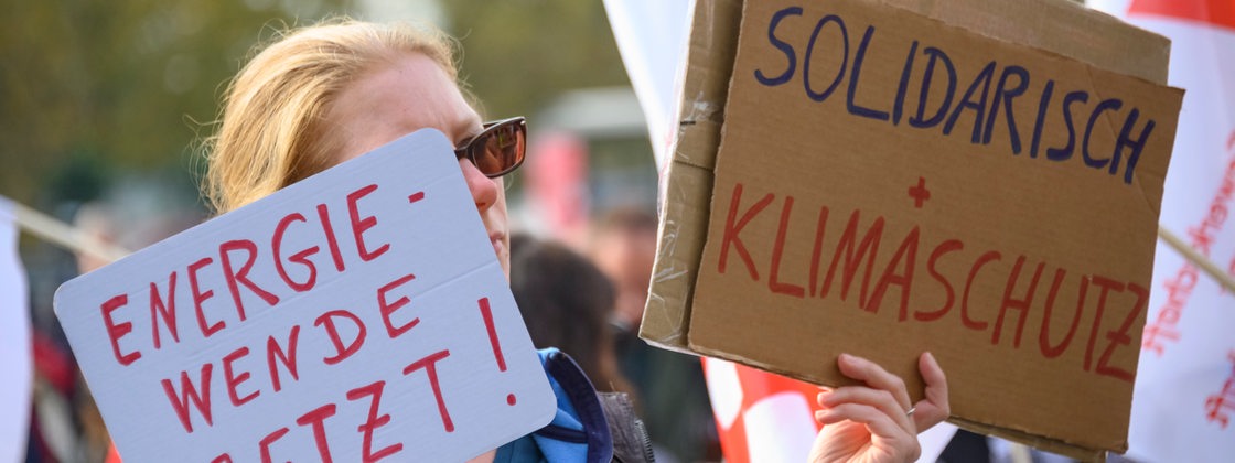 Eine Teilnehmerin hält bei einer Demonstration in der Dresdner Innenstadt im Rahmen der Veranstaltung "Solidarischer Herbst" Schilder mit der Aufschrift "Energiewende jetzt!" und "Solidarisch + Klimaschutz!.