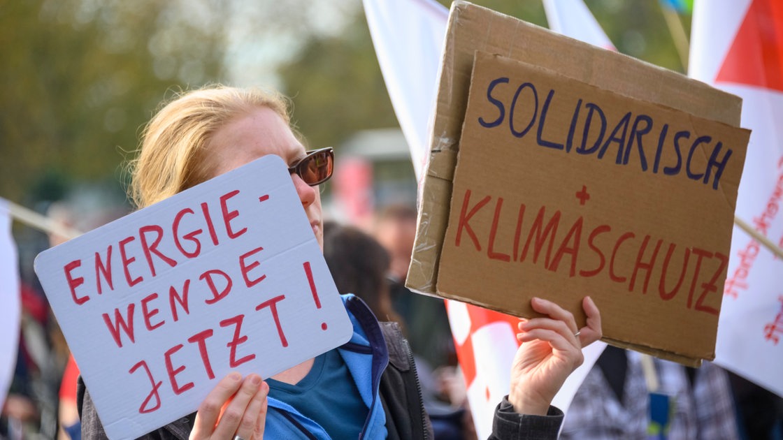 Eine Teilnehmerin hält bei einer Demonstration in der Dresdner Innenstadt im Rahmen der Veranstaltung "Solidarischer Herbst" Schilder mit der Aufschrift "Energiewende jetzt!" und "Solidarisch + Klimaschutz!.