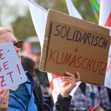 Eine Teilnehmerin hält bei einer Demonstration in der Dresdner Innenstadt im Rahmen der Veranstaltung "Solidarischer Herbst" Schilder mit der Aufschrift "Energiewende jetzt!" und "Solidarisch + Klimaschutz!.