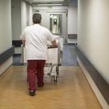 Ein Pfleger schiebt einen Patienten im Krankenbett durch einen Flur