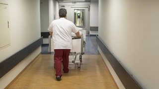 Ein Pfleger schiebt einen Patienten im Krankenbett durch einen Flur