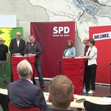 Mehrere Bremer Politiker stehen auf einem Podest. Hinter ihnen sind Aufsteller mit den Farben und Logos ihrer Parteien.
