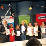 Sieben Personen stehen an einem Tisch und mit dem neuen Koalitionsvertrag zwischen SPD, Grünen und Linken.