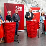 Bremens Bürgermeister Andreas Bovenschulte und weitere Politiker von SPD, Grünen und Linken stehen während eines Pressetermins an Stehttischen.