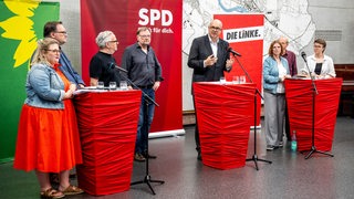Bremens Bürgermeister Andreas Bovenschulte und weitere Politiker von SPD, Grünen und Linken stehen während eines Pressetermins an Stehttischen.