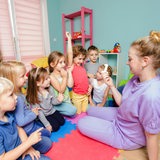 Eine junge Erzieherin sitzt mit einer Kindergruppe auf dem Boden