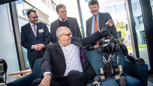 Andreas Bovenschulte (vorne, SPD), Bürgermeister von Bremen, sitzt im Deutschen Forschungszentrum für Künstliche Intelligenz (DFKI) in Bremen neben einem Robotor mit dem Namen Charlie.