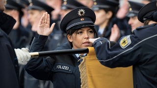 Mit erhobener rechter Hand legt eine Polizistin auf ihrer Vereidigunsfeier ihren Diensteid ab.