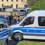 Viele Polizeiwagen stehen vor einem alten Gebäude in Sachsen, Polizeibeamte bewegen sich zwischen den Fahrzeugen.