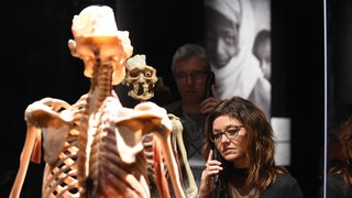 Frau steht in Ausstellung mit Telefon vor einem Skelett