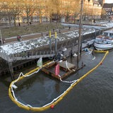 Das Bild zeigt einen Anleger, an dem der Mast und die Dachaufbauten eines Bootes aus dem Wasser schauen.