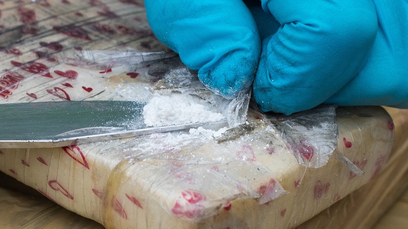 Ein Zollbeamte präsentiert eine Messerspitze der Droge Kokain aus einem sichergestellten Paket.