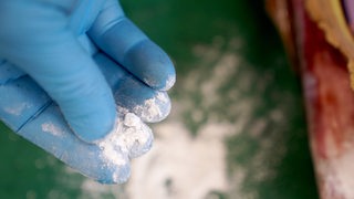 Eine Hand im Handschuhe berührt weißes Kokainpulver.