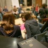 Jugendliche sitzen im Kreis während eines Konfirmandenunterrichtes , im Vordergrund liegt auf einem Tisch eine Bibel. 