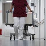 Eine Krankenpflegerin und ein Krankenpfleger schieben ein Krankenbett durch den Gang einer Station eines Krankenhauses.
