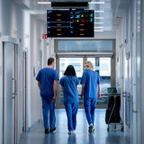 Krankenhauspersonal, von hinten gesehen, geht über einen Klinikflur (Symbolbild)