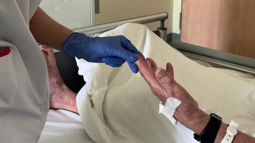 Die Pflegekraft im Bremerhvener Krankenhaus hält die Hand eines älteren Patienten.