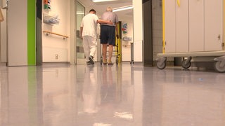 Ein Pfleger begleitet einen alten Mann durchs Krankenhaus.