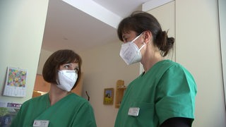 Zwei Frauen in grünen Arbeitskitteln in einem Krankenhaus.