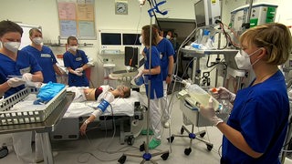 Eine Statistin liegt während einer Notfallübung auf einer Liege im Krankenhaus und ist von Ärzten umgeben.